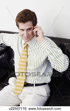 Stock Photograph - High angle view of a businessman sitting on a couch and talking on a mobile phone. Fotosearch