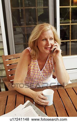 High angle view of a mature woman sitting at the table and talking on a mobile phone View Large Photo Image Stock Photo - High angle view of a mature woman sitting at the table and talking on a mobile phone. Fotosearch
