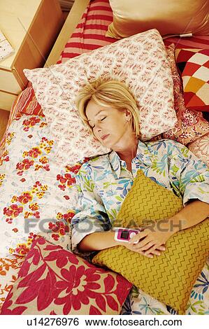 High angle view of a mature woman sleeping on the bed holding a mobile phone View Large Photo Image Stock Photograph - High angle view of a mature woman sleeping on the bed holding a mobile phone. Fotosearch