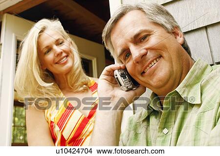 Low angle view of a mature man talking on a mobile phone with a mature woman smiling behind him View Large Photo Image Picture - Low angle view of a mature man talking on a mobile phone with a mature woman smiling behind him. Fotosearch