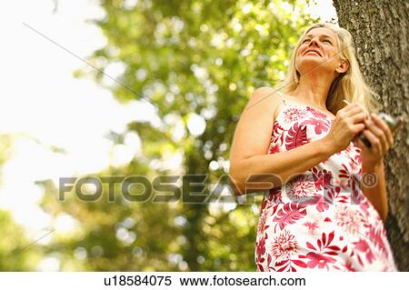 Stock Photography - Low angle view of a mature woman holding a mobile phone and smiling. Fotosearch