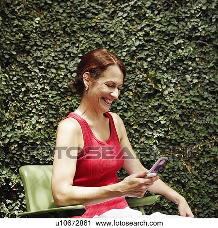 Stock Image - Side profile of a mature woman holding a mobile phone and smiling. Fotosearch