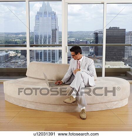 Stock Image - Businessman sitting on a couch and using a laptop. Fotosearch