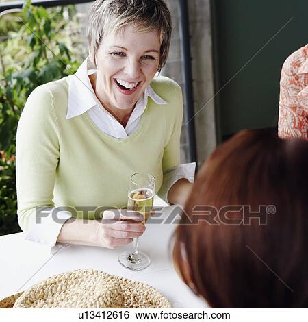 Stock Photograph - Close-up of a mature woman with her friend sitting at the table and smiling. Fotosearch