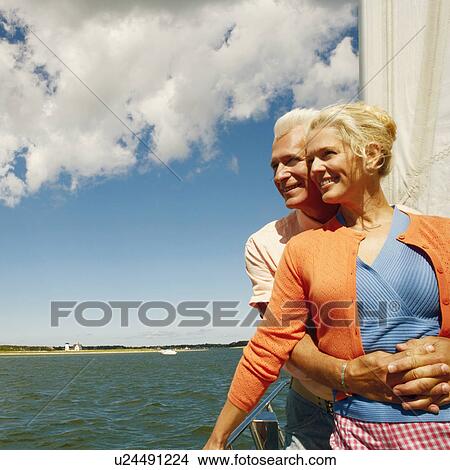 Mature man embracing a mature woman from behind in a sailboat and smiling View Large Photo Image Picture - Mature man embracing a mature woman from behind in a sailboat and smiling. Fotosearch