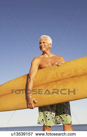 Stock Photo - Mature man holding a surfboard under his arm. Fotosearch