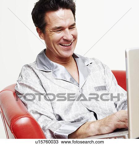 Stock Image - Mature man sitting in an armchair with a laptop and smiling. Fotosearch