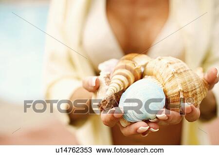 Stock Image - Mid section view of a woman holding conch shells. Fotosearch