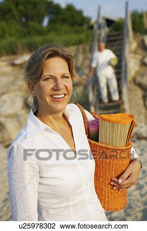 Portrait of a mature woman carrying a beach mat and smiling on the beach View Large Photo Image Stock Image - Portrait of a mature woman carrying a beach mat and smiling on the beach. Fotosearch