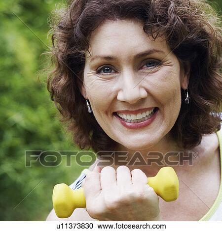 Stock Image - Portrait of a mature woman exercising with a dumbbell and smiling. Fotosearch