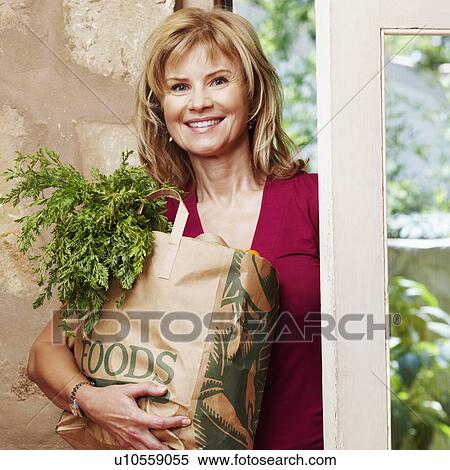 Stock Photography - Portrait of a mature woman holding a shopping bag and smiling. Fotosearch