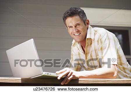 Stock Photograph - Portrait of a mid adult man using a laptop. Fotosearch