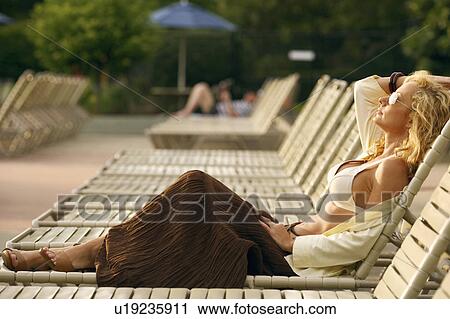 Stock Image - Side profile of a mature woman reclining on a lounge chair. Fotosearch