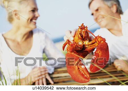 Close-up of a mature man holding a lobster with a mature woman sitting beside him View Large Photo Image Stock Image - Close-up of a mature man holding a lobster with a mature woman sitting beside him. Fotosearch
