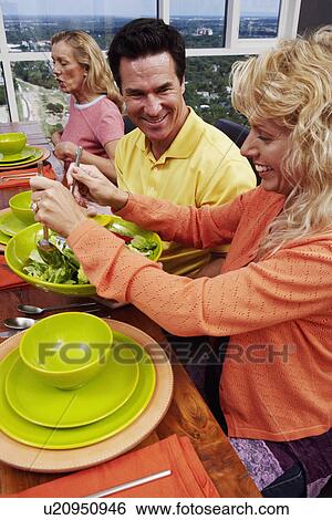 Stock Photograph - High angle view of a mature woman and a mature man with a mid adult woman sitting at the dining table. Fotosearch