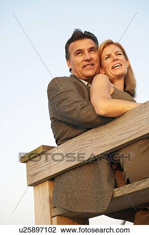 Stock Image - Low angle view of a mid adult woman and a mature man sitting by a railing. Fotosearch