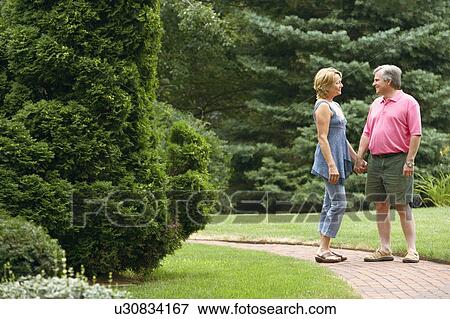 Stock Photo - Mature couple holding hands and smiling in a park. Fotosearch