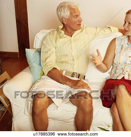 Stock Photograph - Mature couple sitting on a couch and talking to each other. Fotosearch