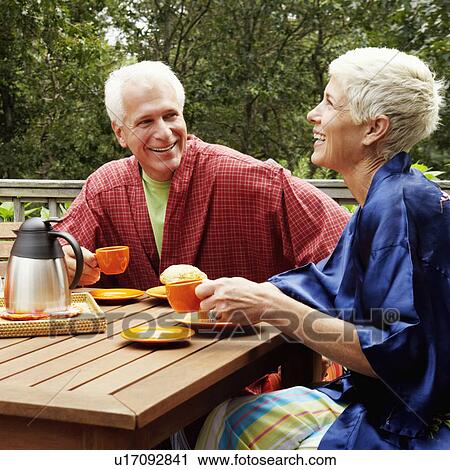 Stock Image - Mature man and a senior woman sitting at the table and smiling. Fotosearch