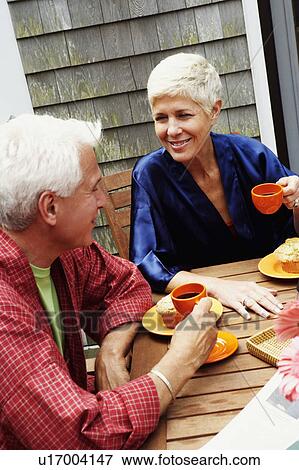 Stock Photo - Mature man and a senior woman sitting at the table and talking to each other. Fotosearch