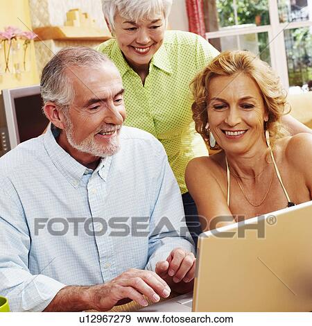 Mature man using a laptop with a mature woman and a senior woman smiling near him View Large Photo Image Stock Photo - Mature man using a laptop with a mature woman and a senior woman smiling near him. Fotosearch