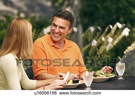 Stock Photograph - Mature man with a mid adult woman sitting at the table and smiling. Fotosearch