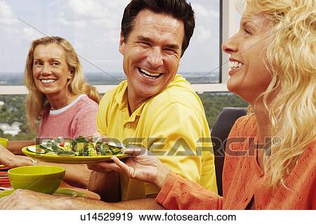 Mid adult woman holding a plate of salad and sitting with a mature couple at the table View Large Photo Image Stock Photo - Mid adult woman holding a plate of salad and sitting with a mature couple at the table. Fotosearch