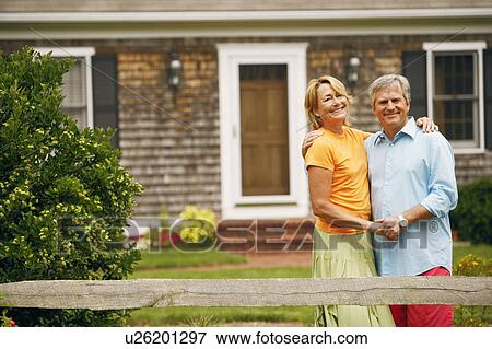 Portrait of a mature couple standing with their arms around each other in front of a house View Large Photo Image Stock Photo - Portrait of a mature couple standing with their arms around each other in front of a house. Fotosearch