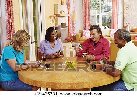 Stock Image - Two mature couples sitting at the table and playing cards. Fotosearch
