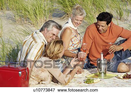 Two mature couples sitting on the beach and holding champagne flutes View Large Photo Image Stock Photo - Two mature couples sitting on the beach and holding champagne flutes. Fotosearch