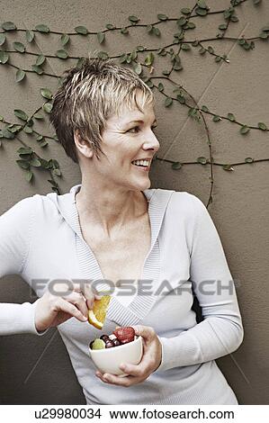 Picture - Close-up of a mature woman smiling and holding a bowl of fruit. Fotosearch