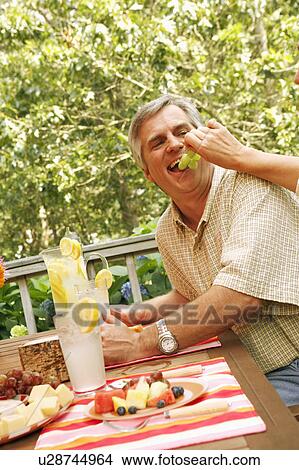 Picture - Close-up of a woman's hand feeding grapes to a mature man. Fotosearch