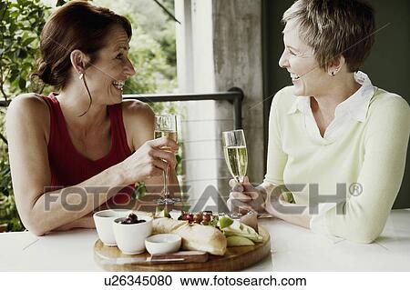 Close-up of two mature women holding champagne flutes and smiling View Large Photo Image Stock Image - Close-up of two mature women holding champagne flutes and smiling. Fotosearch