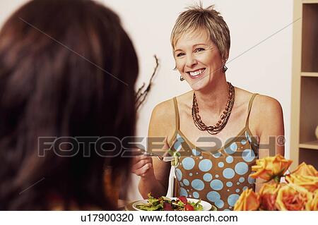 Stock Image - Mature woman eating salad with her friend. Fotosearch