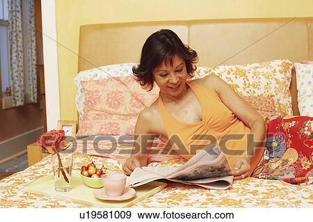 Mature woman lying on the bed and reading a newspaper View Large Photo Image Stock Photo - Mature woman lying on the bed and reading a newspaper. Fotosearch