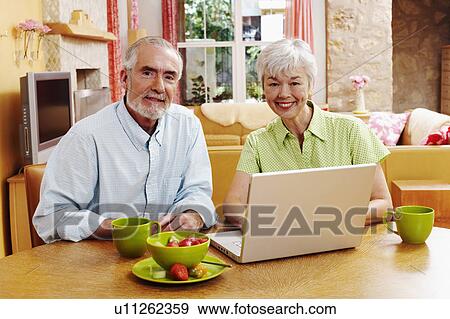 Stock Photo - Portrait of a mature man and a senior woman sitting in front of a laptop and smiling. Fotosearch