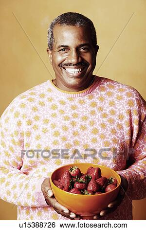 Stock Photograph - Portrait of a mature man holding a bowl of strawberries and smiling. Fotosearch