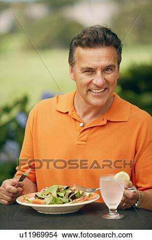 Picture - Portrait of a mature man sitting at the table with a plate of vegetable salad in front of him. Fotosearch