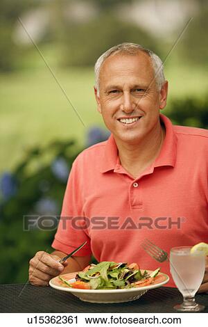 Stock Image - Portrait of a mature man sitting at the table with a plate of vegetable salad in front of him. Fotosearch