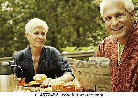 Portrait of a mature man smiling and holding a newspaper with a senior woman in the background View Large Photo Image Stock Image - Portrait of a mature man smiling and holding a newspaper with a senior woman in the background. Fotosearch