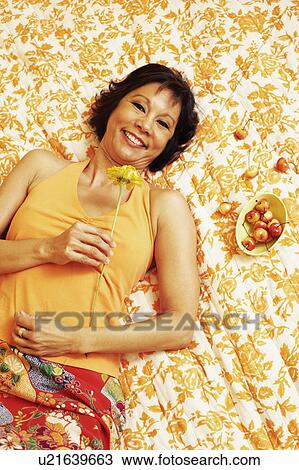 Portrait of a mature woman lying on the bed and holding a flower View Large Photo Image Stock Image - Portrait of a mature woman lying on the bed and holding a flower. Fotosearch