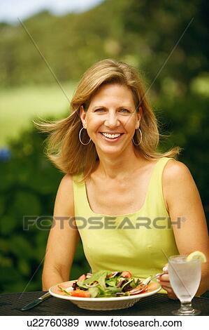 Stock Photo - Portrait of a mature woman sitting at the table with a plate of vegetable salad in front of her. Fotosearch