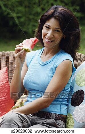 Portrait of a mature woman sitting on a couch and holding a slice of watermelon View Large Photo Image Stock Image - Portrait of a mature woman sitting on a couch and holding a slice of watermelon. Fotosearch