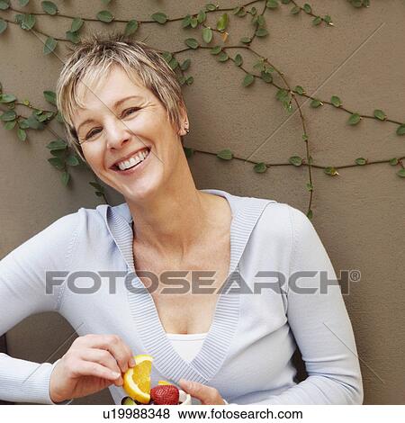 Stock Photo - Portrait of a mature woman smiling and holding a bowl of fruit. Fotosearch