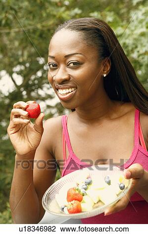 Stock Image - Portrait of a mid adult woman holding a bowl of fruit salad and smiling. Fotosearch