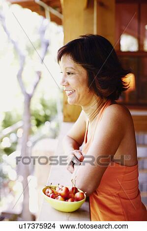 Side profile of a mature woman standing in a balcony with a bowl of cherries beside her View Large Photo Image Picture - Side profile of a mature woman standing in a balcony with a bowl of cherries beside her. Fotosearch
