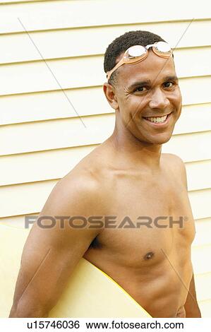 Stock Photograph - Portrait of a mature man carrying a surfboard and smiling. Fotosearch