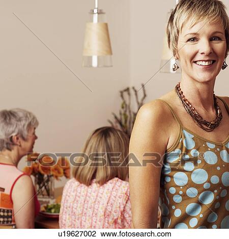 Stock Image - Portrait of a mature woman smiling and her friends sitting at the dining table in the background. Fotosearch