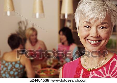 Stock Photo - Portrait of a mature woman smiling and her friends sitting behind her. Fotosearch