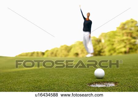 Close-up of a golf ball on the edge of a hole with a man standing in the background View Large Photo Image Stock Photo - Close-up of a golf ball on the edge of a hole with a man standing in the background. Fotosearch